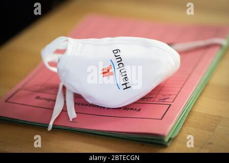 Hamburg, Deutschland. Mai 2020. Auf einer Dokumentenmappe des Hamburger Bildungssenators Rabe auf einer Pressekonferenz in der Grundschule Wielandstraße liegt ein Mund-Nase-Cover mit dem Hamburger Logo. Nach drei Monaten Urlaub und Online-Unterricht sollen alle Hamburger Schüler diese Woche wieder ihre Lehrer besuchen. Kredit: Christian Charisius/dpa/Alamy Live News Stockfoto