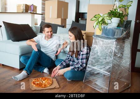 Glückliche Familie, die Pizza am Tag des Umzugss isst. Bild eines jungen Paares, das sich im neuen Haus ausruhen kann Stockfoto
