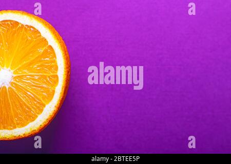 Eine halbe orange Nahaufnahme auf einem hellen violetten Hintergrund. Saftiges Sommerkonzept mit Kopierfläche. Stockfoto