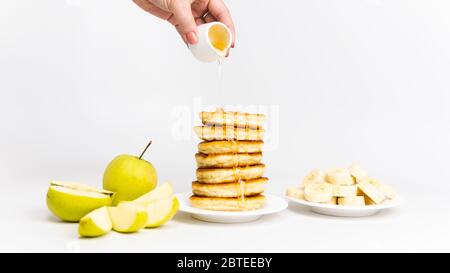 Süße hausgemachte Pfannkuchen mit Banane, Apfel und Honig oder Ahornsirup auf weißem Hintergrund, Nahaufnahme. Konzepte für Frühstück, Snacks und richtige Ernährung. Stockfoto