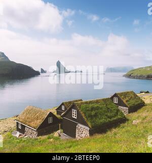 Malerischer Blick auf die traditionellen färöischen Grashäuser im Dorf Bour. Drangarnir und Tindholmur Meer stapeln sich im Hintergrund. Vagar-Insel, Färöer, Dänemark. Landschaftsfotografie