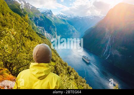 Atemberaubende Aussicht auf den Sunnylvsfjord und die berühmten Wasserfälle der Seven Sisters, in der Nähe des Dorfes Geiranger im Westen Norwegens. Tourist in gelben Jacke am Rand des Felsens. Landschaftsfotografie Stockfoto