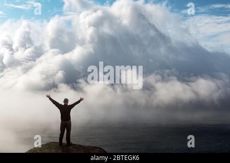 Silhouette eines Mannes mit erhobenen Armen am Rand einer Klippe über einem nebeligen Ozean. Reisekonzept. Landschaftsfotografie Stockfoto