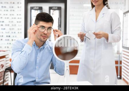 Spezialist hilft jungen Mann, Brille zu wählen Stockfoto
