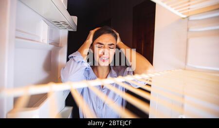 Verzweifelte Hausfrau in Verzweiflung Blick auf leeren Kühlschrank Stockfoto