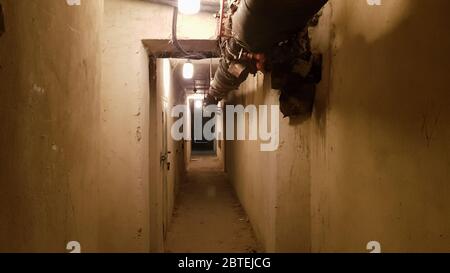Ein dunkler Keller, ein langer Korridor mit alten rostigen Metalltüren und Rohren. Beleuchteter Tunnel in einem Bombenschutzraum, unterirdischer Militärbunker des Kalten Krieges, per Stockfoto