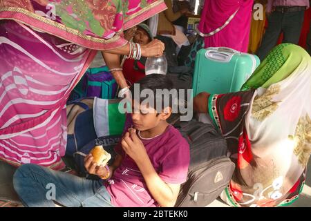 Auf einem Bahnsteig in Mumbai, Indien, sitzt ein Junge umgeben von weiblichen Familienmitgliedern, die populären lokalen Snack oder Street-Food-Artikel Vada Pav essen Stockfoto