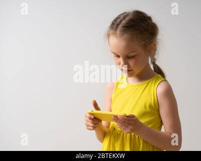 Schöne kleine Mädchen in hellen ärmellosen Kleid mit niedlichen Zopf genießt mit ihrem stilvollen smartpthone. Nahaufnahme Studio-Porträt isoliert auf weiß Stockfoto