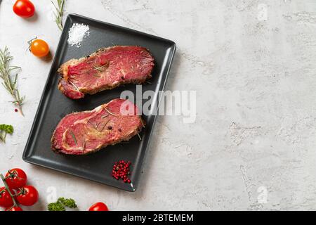 Marinierte rohe Steaks auf Steintisch mit Gewürzen Stockfoto