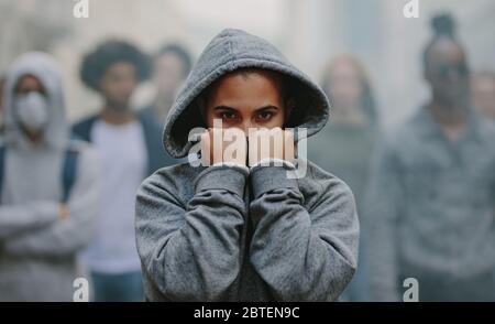 Aktivistin im Kapuzenhemd, die ihr Gesicht mit ihren Händen bedeckt und dabei lautlosen Protest macht. Sozialaktivist protestiert still. Stockfoto