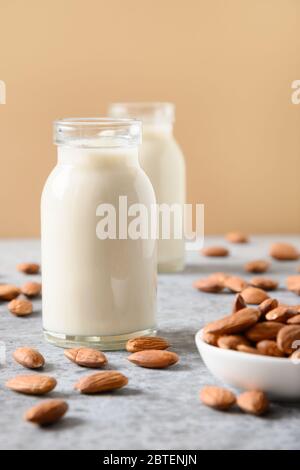 Frische Mandelmilch in Glasflaschen und Mandeln auf beigem Hintergrund. Nahaufnahme. Vertikal. Gesunder veganer Milchersatz. Mangel an Cholesterin. Stockfoto