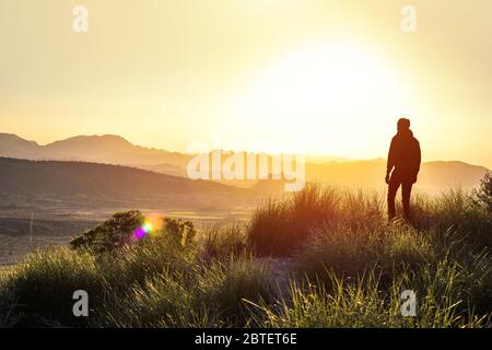 Anonyme Silhouette eines Mannes auf dem Gipfel des Berges vor einer nebligen Landschaft. Erster Mensch in einer anderen Welt. Konzept eines anderen Planeten Entdeckung eines neuen Landes. Stockfoto