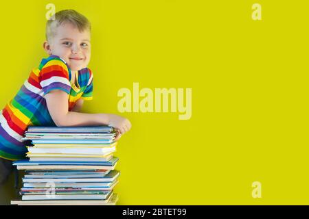 Das Kind hält einen großen Stapel Kinderbücher in seinen Händen. Grüner Hintergrund. Stockfoto