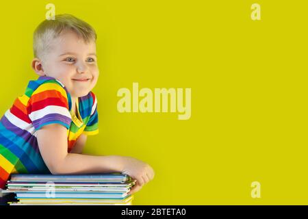 Das Kind hält einen großen Stapel Kinderbücher in seinen Händen. Grüner Hintergrund. Stockfoto
