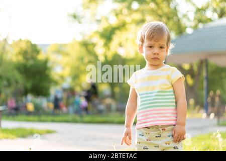 Kindheit, Natur, Sommer, Parks und Outdoor-Konzept - Porträt von niedlichen blonden kleinen Jungen in gestreiften mehrfarbigen T-Shirt mit serous, traurig Stockfoto