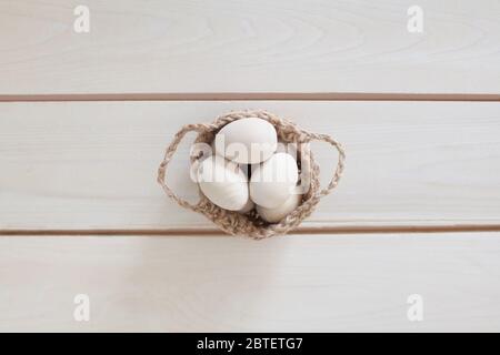 Hölzerne Ostereier in einem Korbgeflecht, gestrickt Korb. Weißer Holzhintergrund. Stockfoto