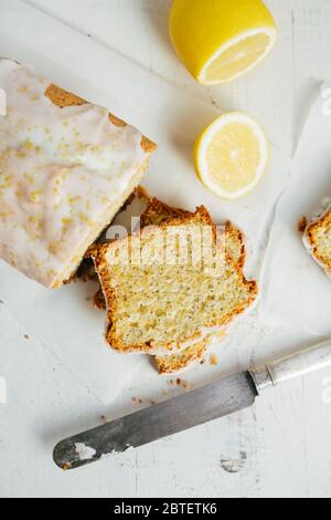 Glasierte Zitrone Pfund Kuchen Laib mit Mohn und Zitronenschale auf einem weißen rustikalen Holztisch. Draufsicht Stockfoto