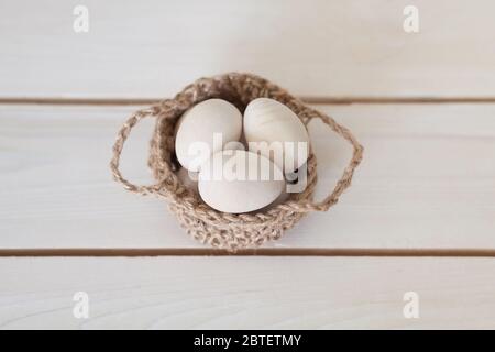 Hölzerne Ostereier in einem Korbgeflecht, gestrickt Korb. Weißer Holzhintergrund. Stockfoto