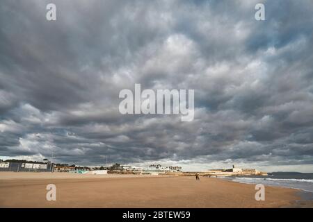 Bild mit niedrigem Horizont vom Strand Carcavellos von Lissabon, Portugal, mit niedrigen Wolken und wenigen Menschen am Strand Stockfoto