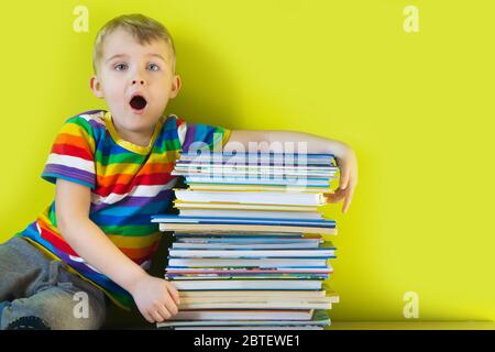 Das Kind hält einen großen Stapel Kinderbücher in seinen Händen. Grüner Hintergrund. Stockfoto
