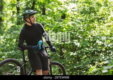 Radsportler, der sich auf dem Fahrrad lehnt und die Flasche mit Wasser hält Stockfoto