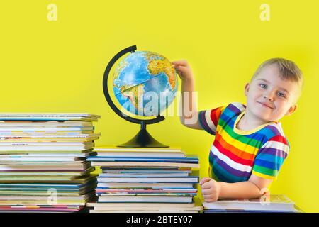 Der Junge sitzt neben den Kinderbüchern und der Welt. Grüner Hintergrund. Stockfoto