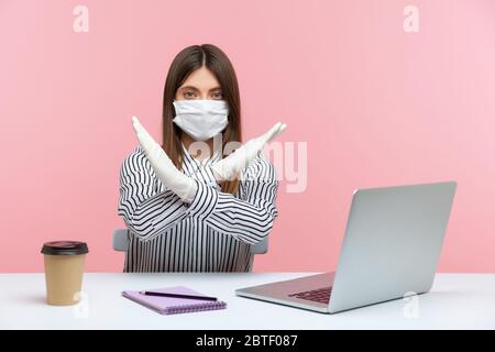 Verbot, Quarantäneverbote. Geschäftsfrau sitzt gesund mit hygienischer Gesichtsmaske und Schutzhandschuhen, zeigt Stop, x Zeichen mit gekreuzten Händen Stockfoto