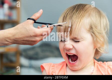 Kleines Mädchen schreiend, während Mutter einen Haarschnitt zu Hause Stockfoto