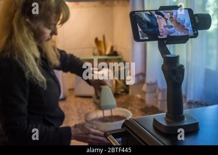 Erwachsene Frau filmt sich selbst, indem sie den Teig mit einem Mixer für einen Kuchen während der Quarantäne vorbereitet. Stockfoto
