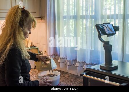 Erwachsene Frau filmt sich selbst, indem sie den Teig mit einem Mixer für einen Kuchen während der Quarantäne vorbereitet. Stockfoto