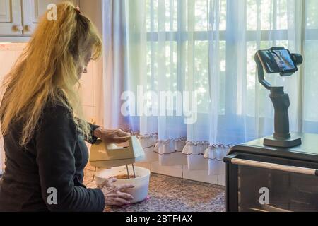 Erwachsene Frau filmt sich selbst, indem sie den Teig mit einem Mixer für einen Kuchen während der Quarantäne vorbereitet. Stockfoto