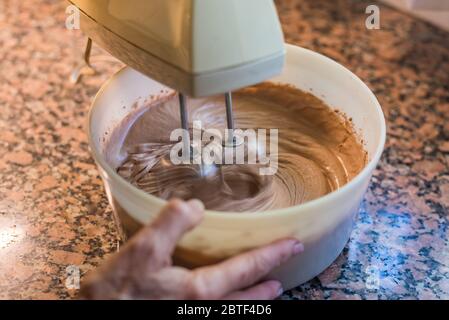 Frauenhand hält eine Schüssel, während sie während der Quarantäne für einen Kuchen mischt Stockfoto