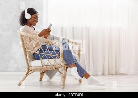 Wochenende Entspannen. Schöne Schwarze Mädchen Im Sessel Entspannen, Musik Auf Dem Smartphone Hören Stockfoto