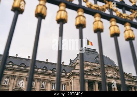 Der Königspalast in Brüssel, Belgien. Blick durch den Metallzaun mit goldenen Details. Nationalflagge des Königreichs Belgien winkt auf der Spitze. Stockfoto