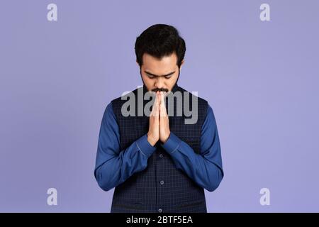 Friedlicher indischer Mann, der auf farbigem Hintergrund zu Gott betet Stockfoto