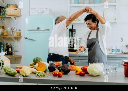 Asiatische ältere Paar tanzen und lächeln in der Küche. 70er Jahre älterer Mann und Frau kochen zusammen zu Hause. Stockfoto