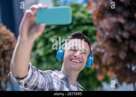 Fröhlicher dunkelhaariger Mann mit Kopfhörern, Selfie machen, lächeln Stockfoto