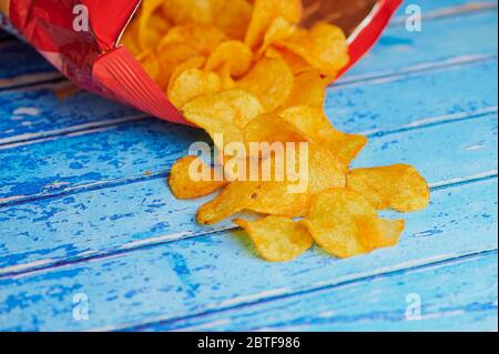 Kartoffelchips liegen vor einem Chips-Beutel vor blauem Hintergrund Stockfoto