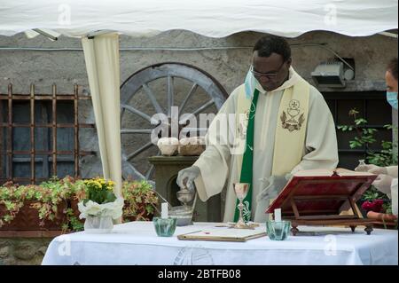 Italien - 2020, Mai 24: Der afrikanische Priester feiert die Messe während der Blockade des Covid-19, mit Handschuhen und Schutzmasken. Stockfoto