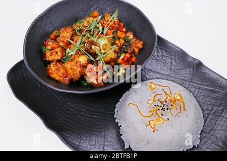 Knusprig gebratenes chinesisches Chilischuhnchen mit Jasminreis in schwarzer Platte Stockfoto