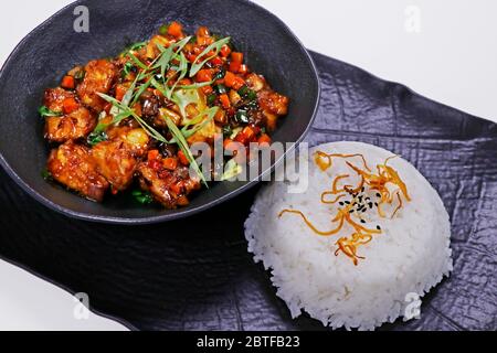 Knusprig gebratenes chinesisches Chilischuhnchen mit Jasminreis in schwarzer Platte Stockfoto