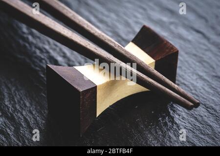 Nahaufnahme eines traditionellen japanischen natürlichen Holzstäbchen, der auf einem Hashioki auf einer schwarzen Schieferoberfläche ruht Stockfoto