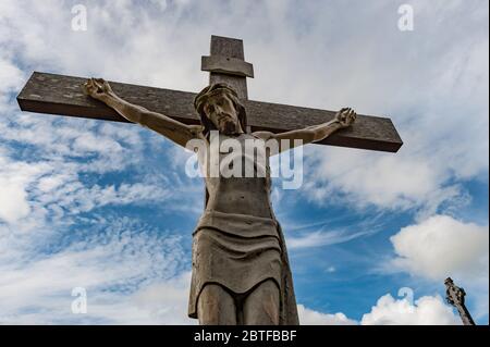 Nahaufnahme der alten verwitterten Jesus Kreuzigungsstatue in einem ländlichen irischen Friedhof, wolkig blauer Himmel Hintergrund Stockfoto