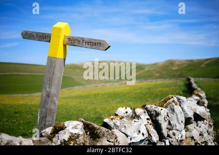 Ein gelb gestrichenes Wanderwegschild in Kalkstein-Landschaft mit Rückendeckung Grüne Wiesen und ein blauer Himmel in der Nähe von Grassington in der Yorkshire Dales National Park Stockfoto