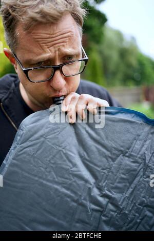 Nahaufnahme von Mann bläst ein selbst aufblasbare Schlafpolster für Camping Stockfoto