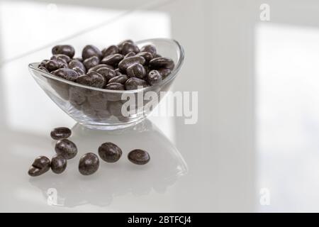 Rosinen in Schokolade in einer Glasschale auf einer glänzenden, hellen Oberfläche Stockfoto