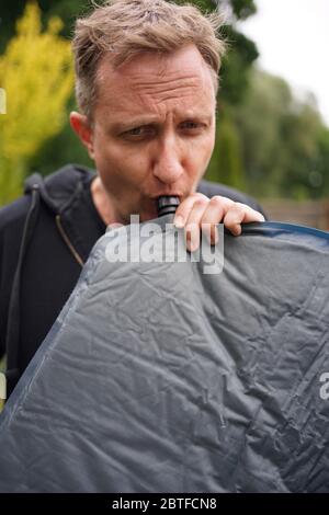 Nahaufnahme von Mann bläst ein selbst aufblasbare Schlafpolster für Camping Stockfoto