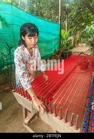 Seidenweberei auf Koh Dach Island, einer Insel vor dem Zentrum von Phnom Penh, Kambodscha. Hier nimmt eine Frau Seidenfäden von Spulen und richtet sie gerade Stockfoto