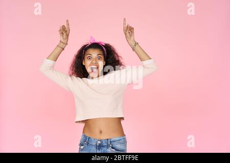 Aufgeregt afrikanischen Teenager-Mädchen zeigen Finger nach oben isoliert auf rosa Hintergrund. Stockfoto