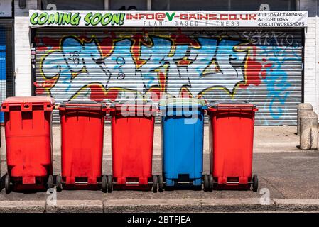 Bunte städtische Straßenszene in Westcliff, Southend on Sea, Essex, Großbritannien. Veganes, pflanzliches Fitnessgeschäft. Geschlossen. Reihe der Mülltonnen. Graffiti. Seltsam Stockfoto